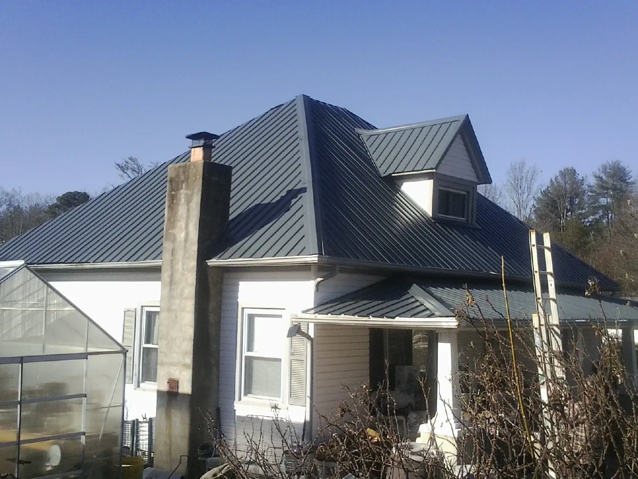 Dark blue standing seam metal roof on a white farmhouse with dormer — Slate & Tile Roof Repair by Roofing Brothers in China Grove