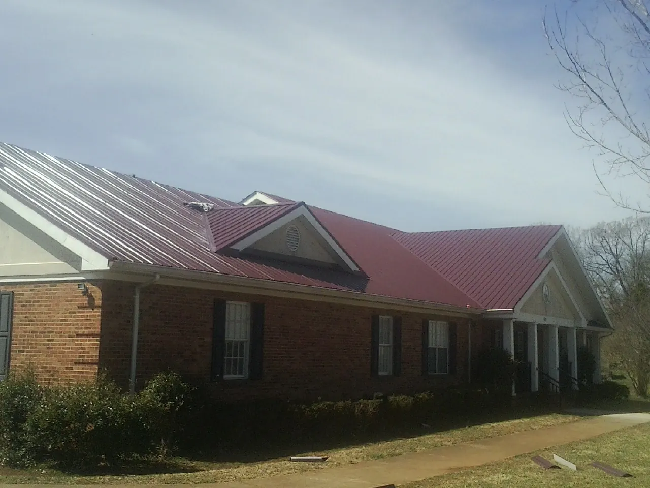 Red metal roof with gabled entries on a long brick building, from a Hail Damage Roof Repair job in China Grove