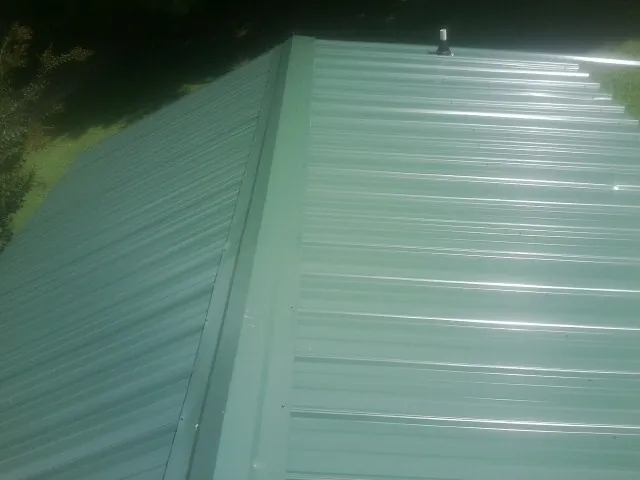 New green metal panels meeting at the ridge of a roof — Flat Roof Repair work by our crew in China Grove