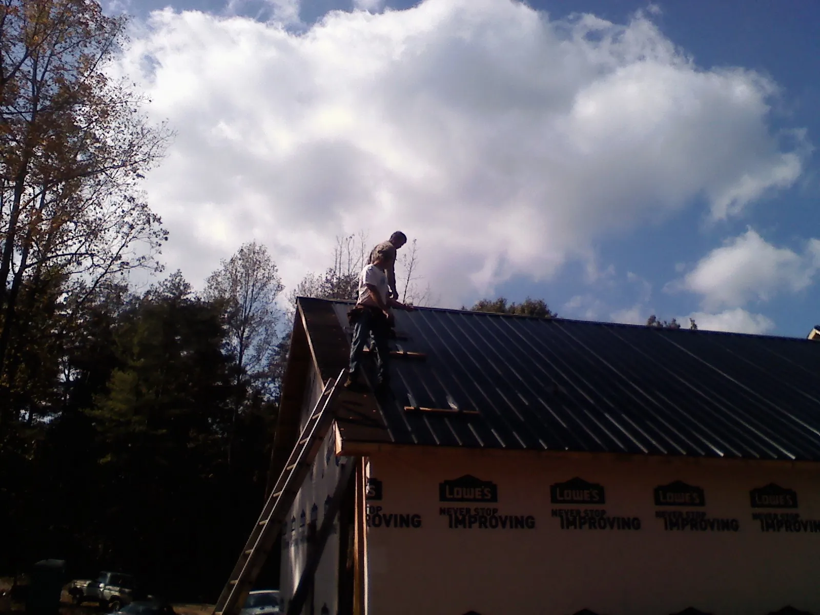 Roofer fastening dark metal panels high against a cloudy sky, from a Roof Inspection job in China Grove