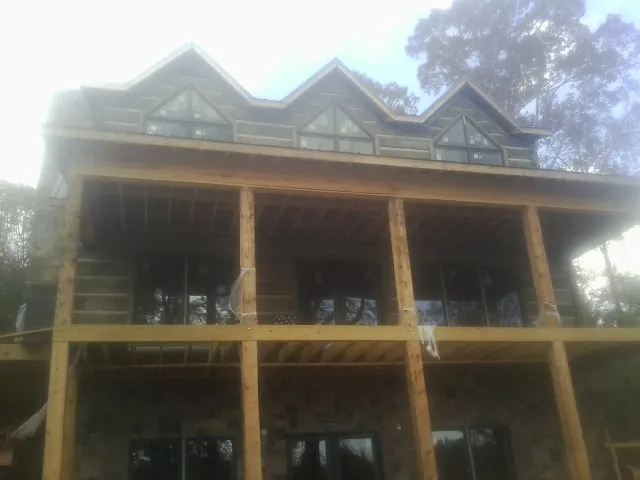 Dormers and porch framing on a large log home under construction — Roof Coating work by our crew in China Grove