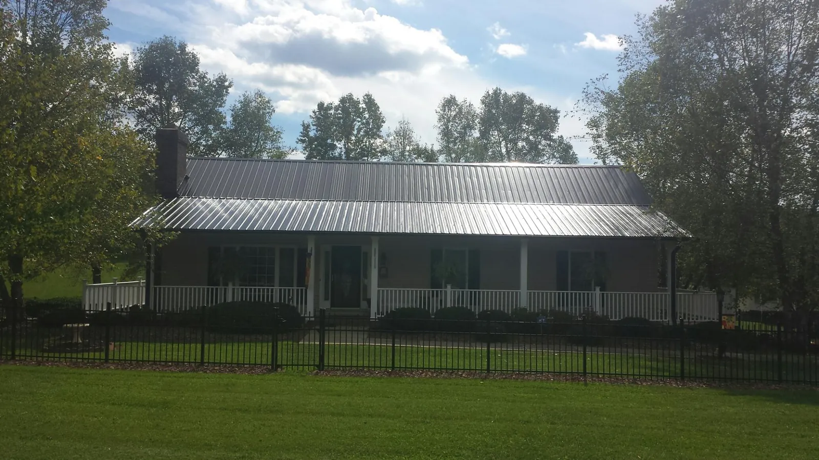 Gray metal roof on a brick ranch with a full width front porch — Gutter Guard Installation work by our crew in China Grove