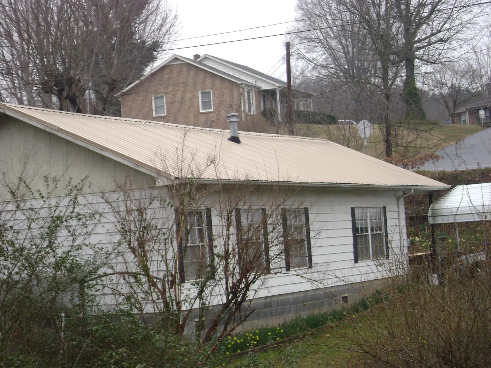Tan metal roof on a white sided house set into a hillside — Commercial Roofing by Roofing Brothers in China Grove
