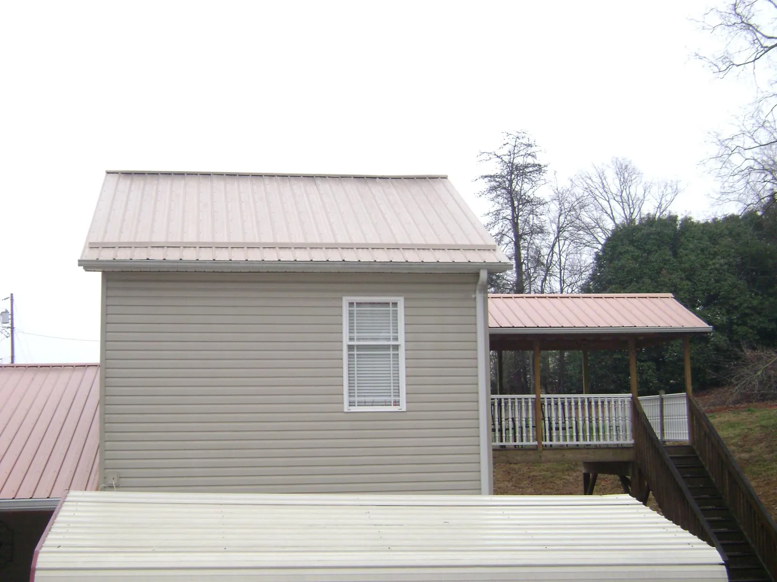 Tan metal roofs on a two story addition and attached porch, from a Roof Replacement job in China Grove